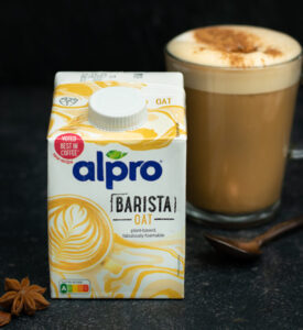 Een brik Alpro Barista Oat met op de achtergrond een glazen mok dirty chai latte.