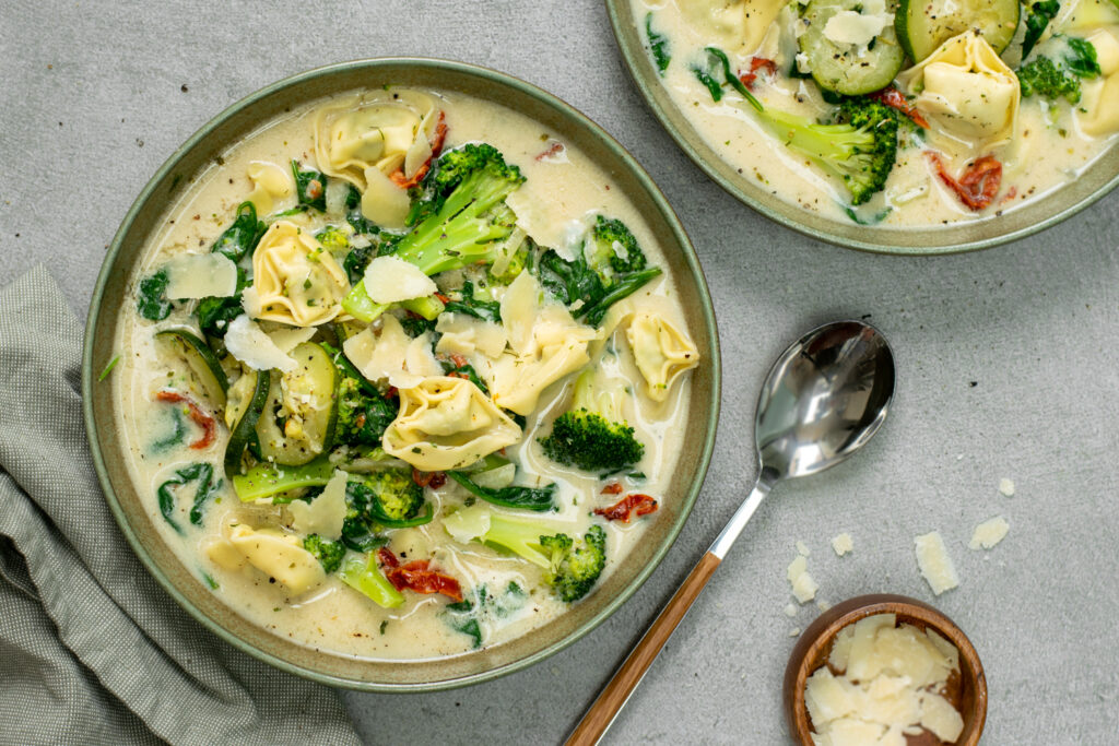 Bovenaanzicht van een lichtgroen diep bord gevuld met een romige tortellinisoep met broccoli en spinazie.